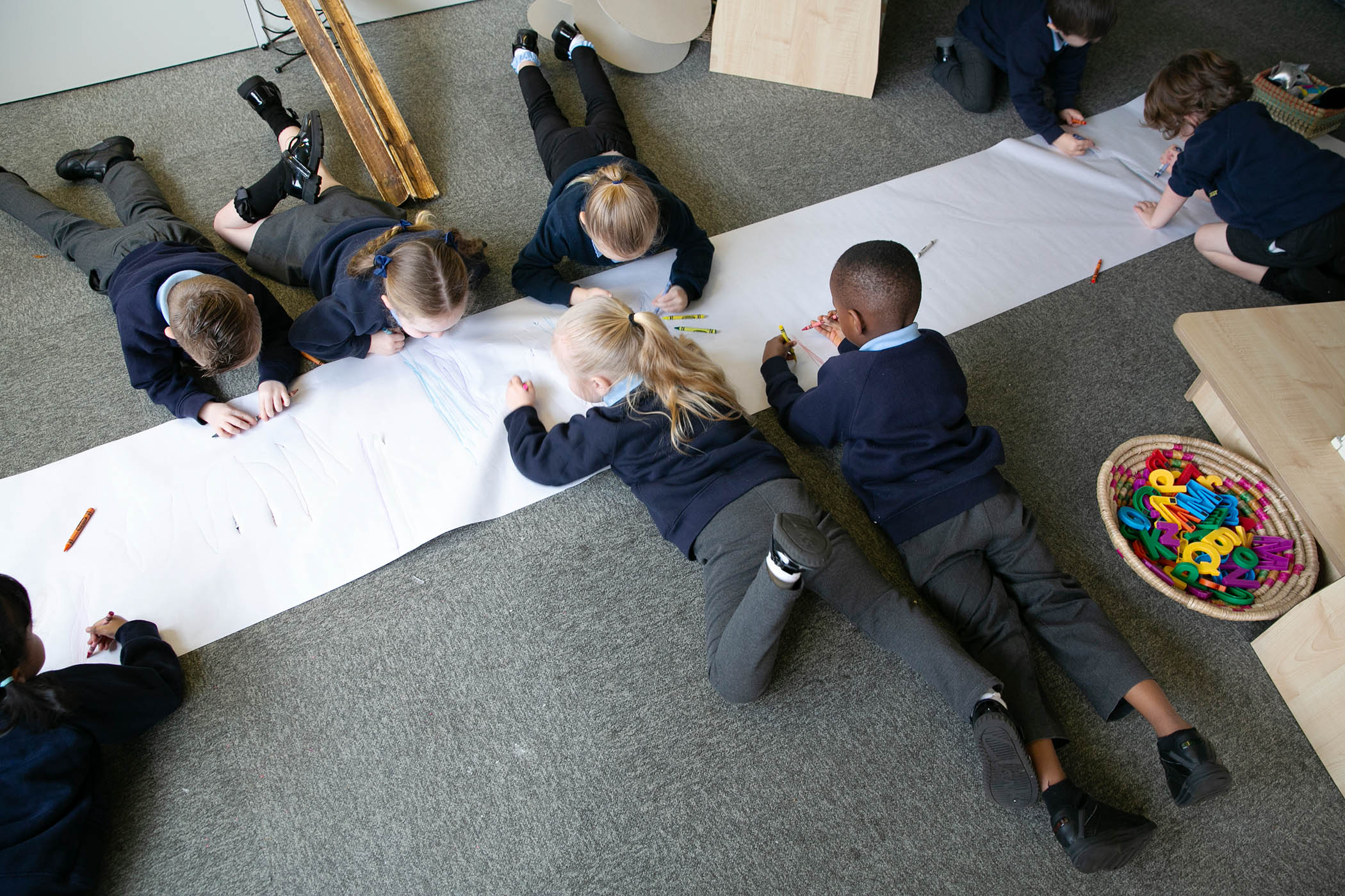 Children lying on their tummies to help core strength using crayons to draw in Reception class at St Peter’s Church of England primary school in Hindley , Wigan in Greater Manchester.