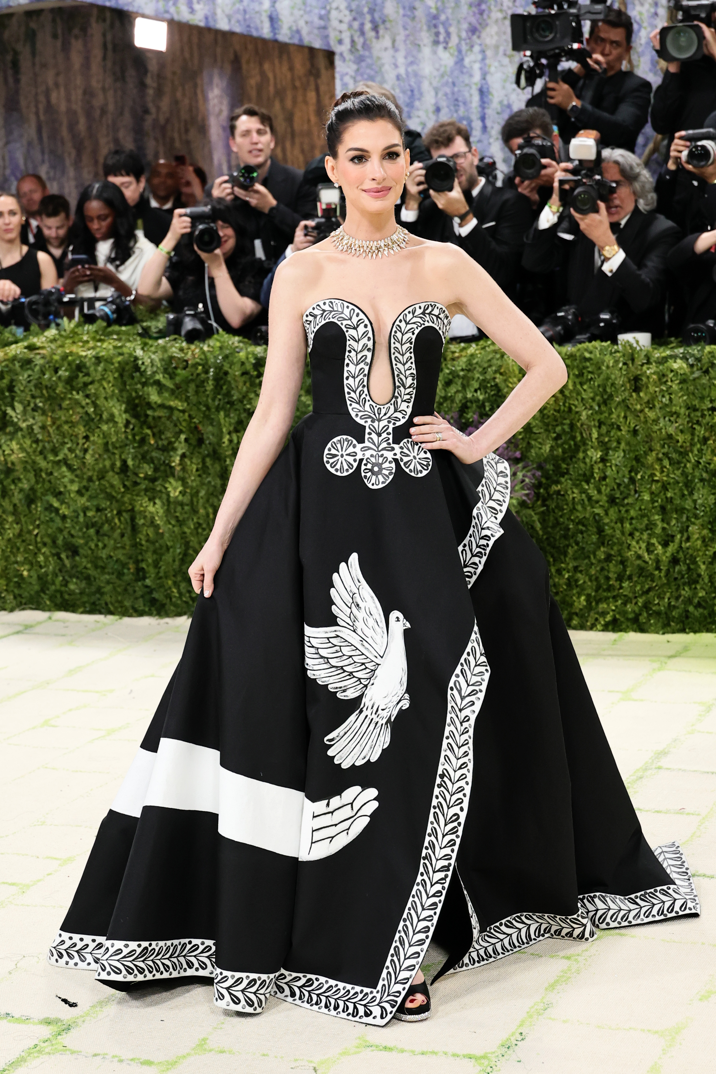 Anne Hathaway’s strapless black Mikado-silk ball gown, complete with a plunging neckline and high-leg slit, was a custom Michael Kors Collection dress. Designed in collaboration with prominent American artist Peter McGough, it served as a sleek canvas for intricate hand-painting work, inspired by the poem Ode on a Grecian Urn by John Keats.