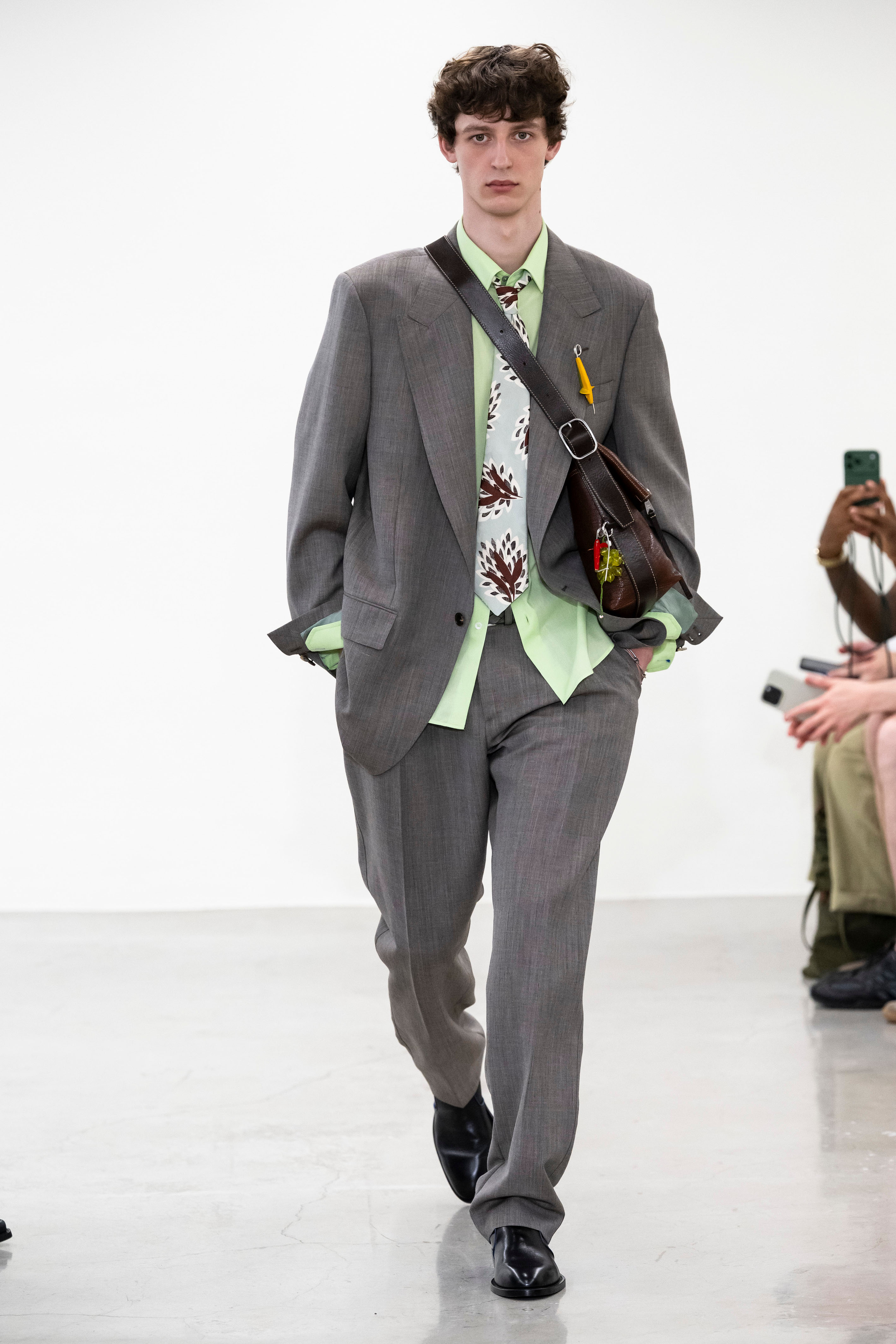 PAUL SMITHIn a preview ahead of his show, Paul Smith delightedly produced an old photo of him as a child with his granddad at Skegness – his grandfather wearing a suit with legs rolled up, paddling. “People used to wear suits all the time,” Smith remarked. The incongruity of the image sparked the collection’s title: Suits in Unsuitable Situations . The SS27 offering references his tailoring work from the 80s and 90s, rediscovered by his design directors following a visit to his Nottingham archive. Smith noted that Gen Z are “interested in nostalgia” and suits are becoming popular again. This collection had the ease and playfulness that Paul Smith is known for; an unlined silhouette resulted in a soft, relaxed look in summer-friendly fabrics like mouliné seersucker, and a Scottish-made tropical-weight wool. Archive tie prints became prints for shirts and summer co-ords. Tapestry samplers from Paul’s love of vintage fairs and collection of knick-knacks inspired the quirky knitwear that shouldn’t work with tailoring, but do. Lapel pins featured flotsam and jetsam charms and hand-painted pebbles were left on guests seats – a nod to Smith’s father, who would bring pebbles home from those family beach trips and decorate them.