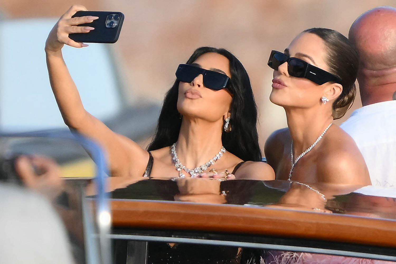 Kim Kardashian (L) and sister Khloe take selfies on the boat heading for the venue.