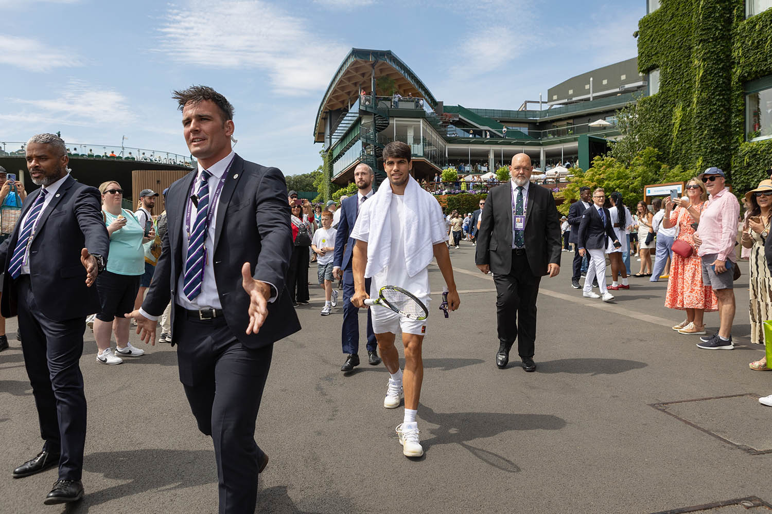 Alcaraz gets an escort to the practice courts through the crowds.