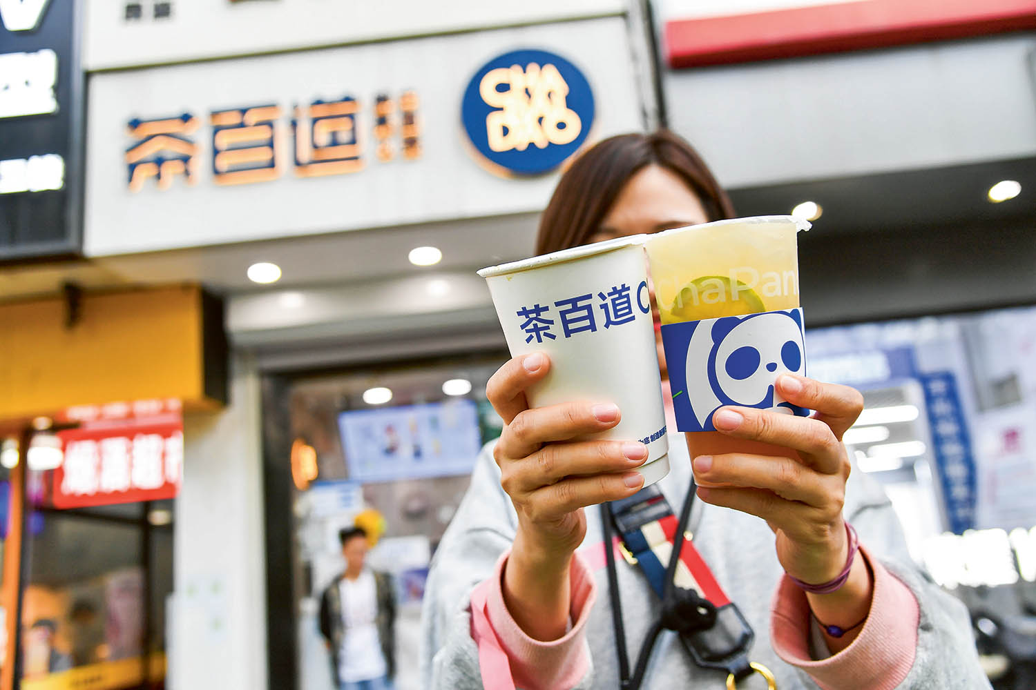 A customer shows her newly purchased milk tea outside Chabaidao bubble tea store in Beijing, China