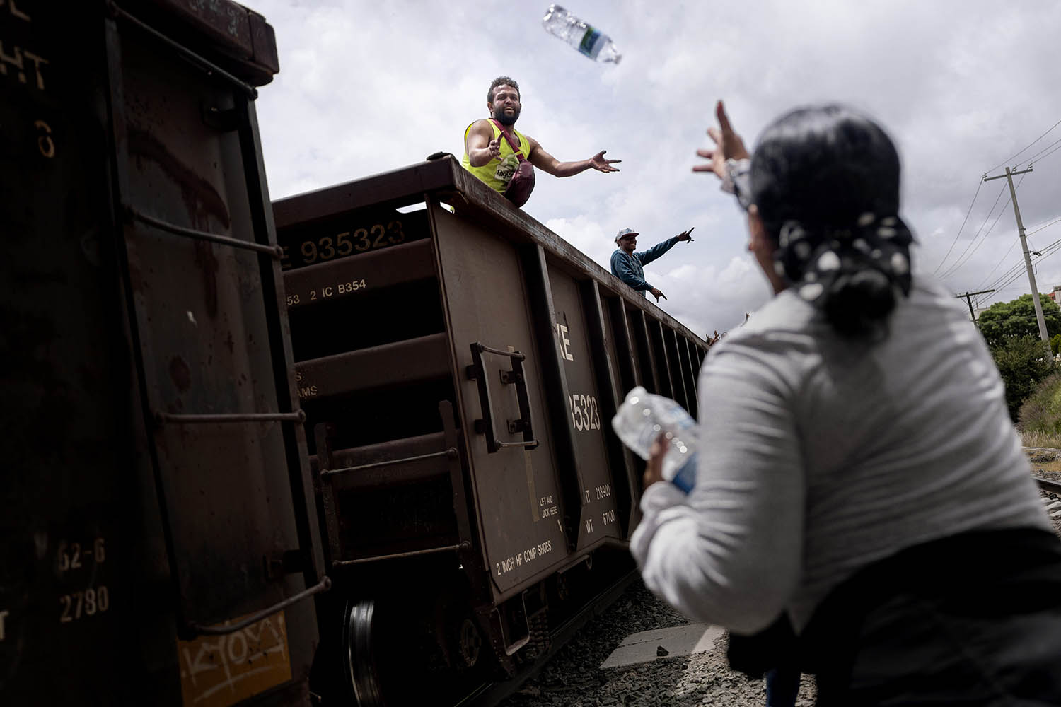 Volunteers from charity, Nueva Esperanza (New Hope) throw bottles of water to migrants on board the freight train