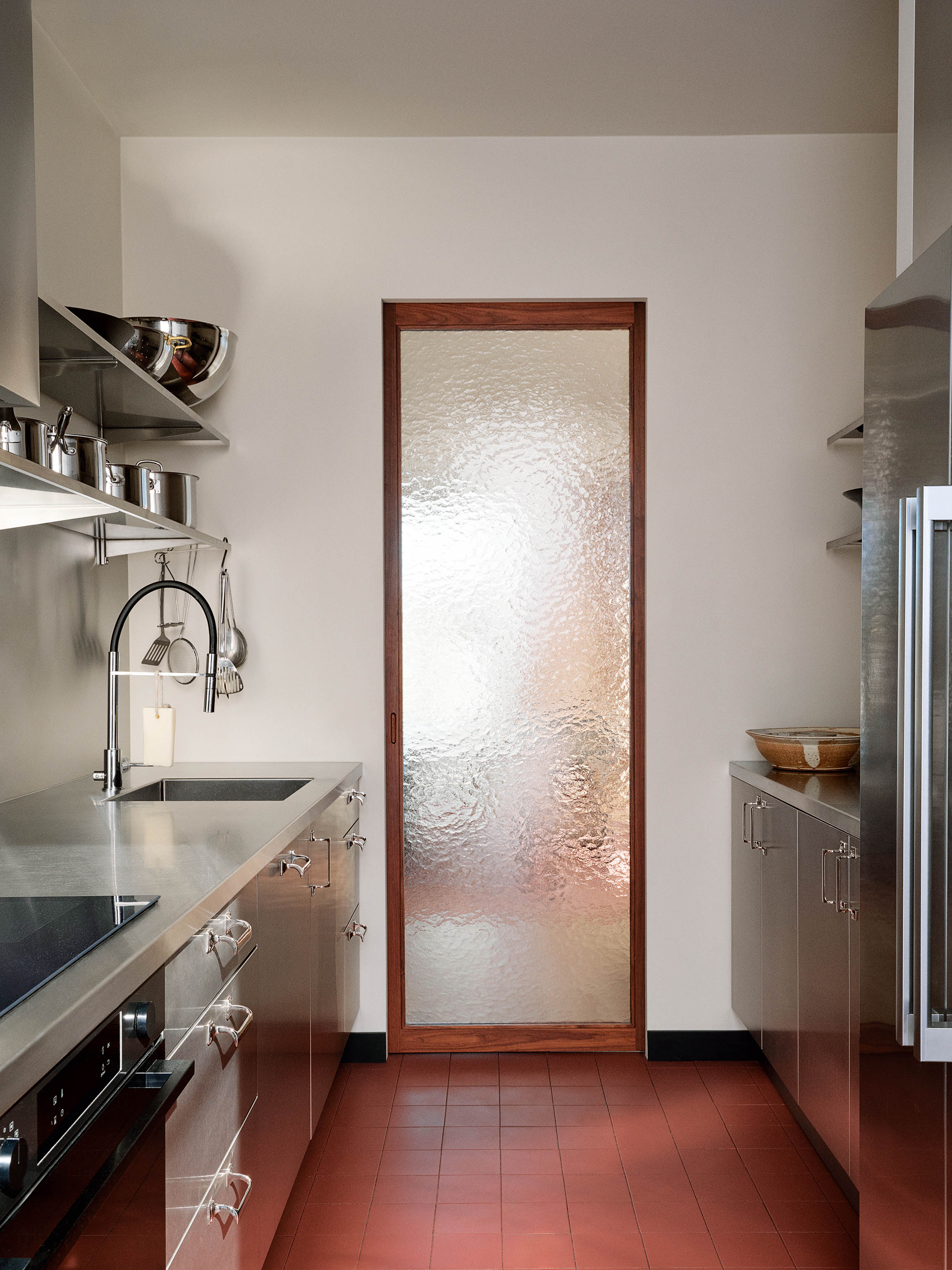 Cooking up a storm: stainless-steel worktops and a tall glass door in the deliberately compact kitchen, which ensures people eat around the table in the dining room