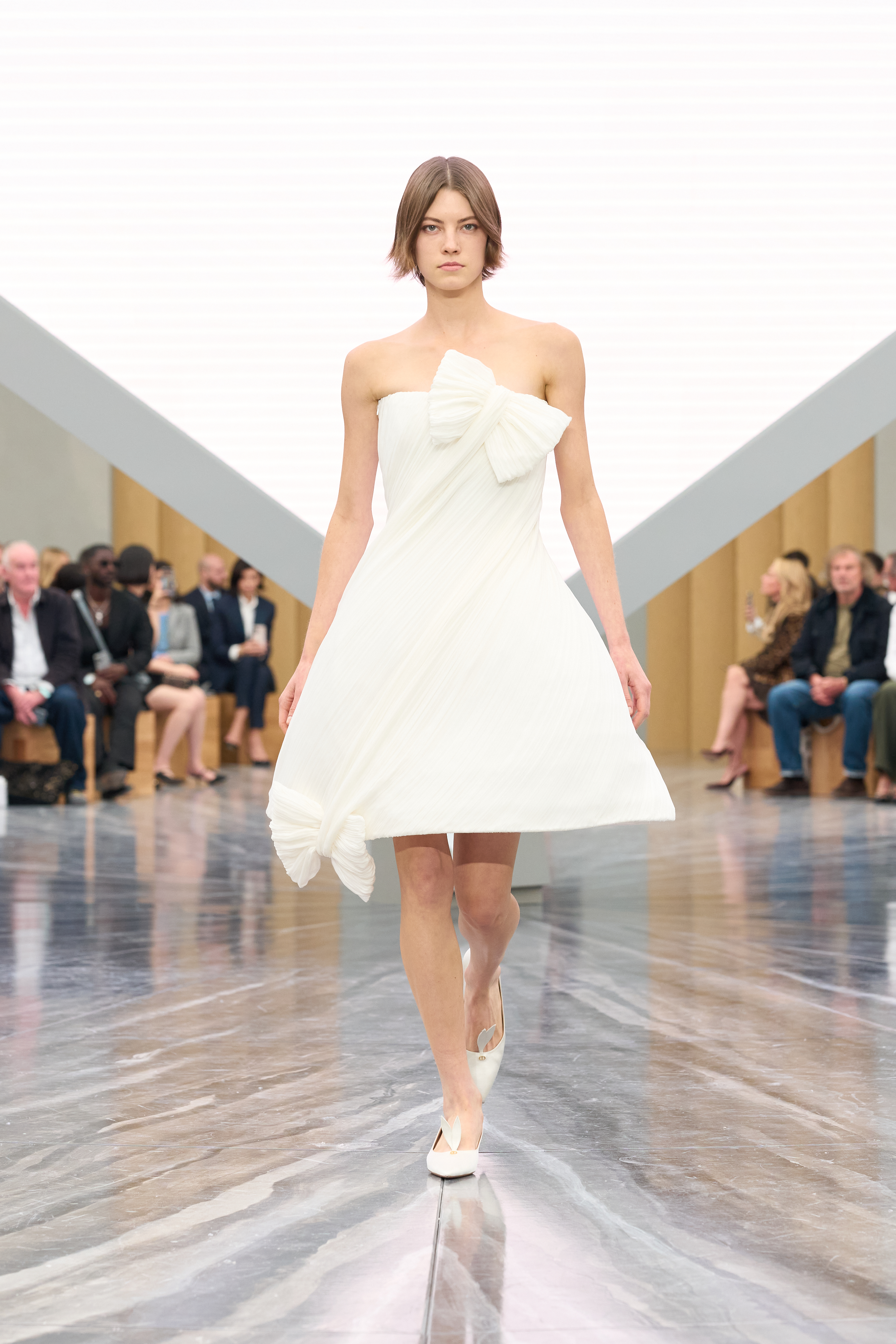 Opening the show , a white bell-shaped dress pieced together on a diagonal, tied into two bows.