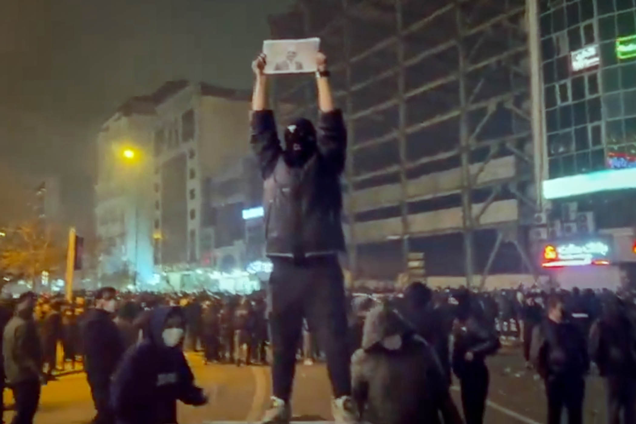 A masked demonstrator holds a picture of Iran’s crown prince Reza Pahlavi