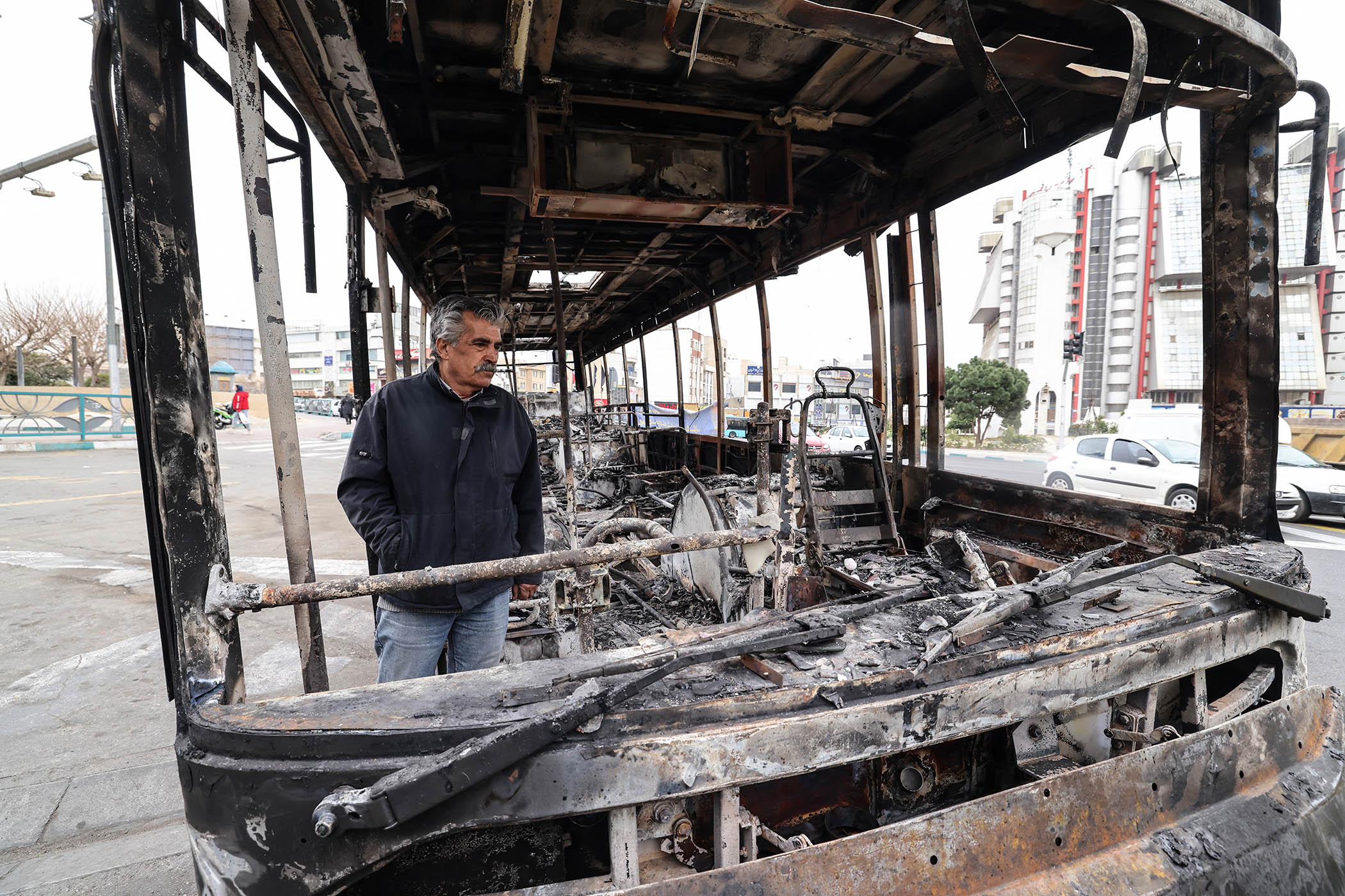 A man stands in the wreckage of a bus in Tehran’s Sadeghieh Square that was burned by protesters demonstrating against economic hardship