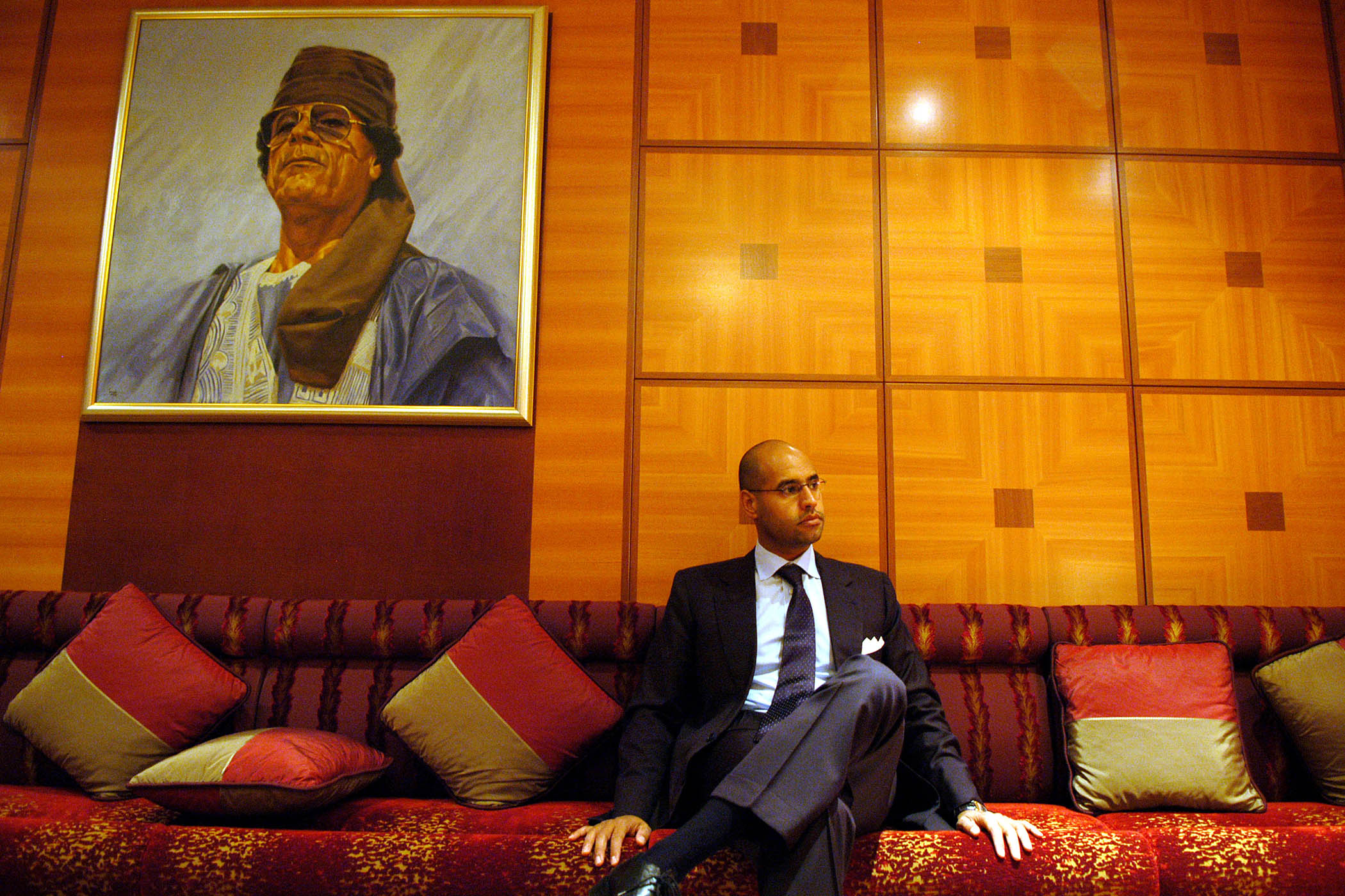 Saif al-Islam sits under a portrait of his father, Muammar Gaddafi, during an interview in Tripoli in 2004