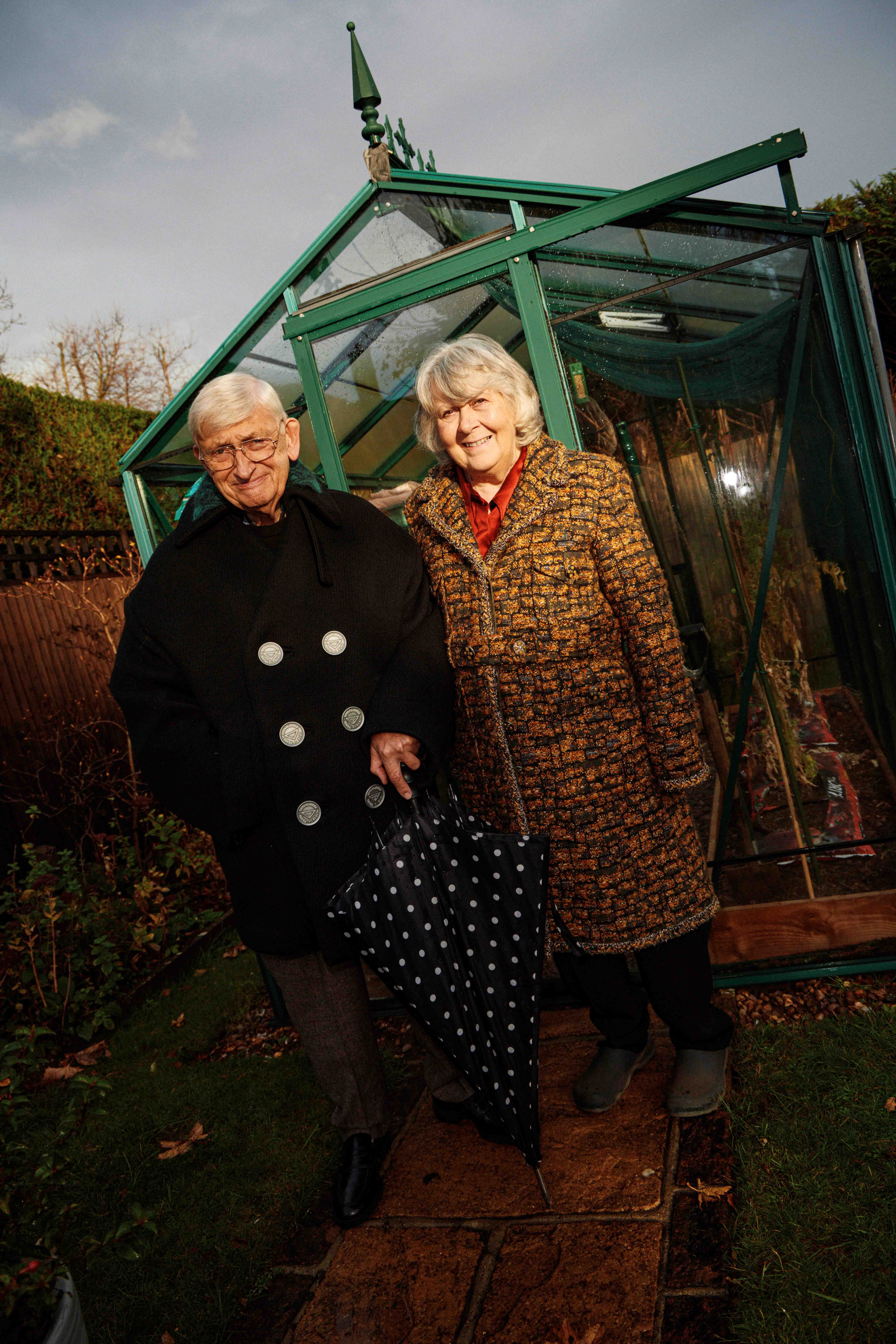 Michael wears peacoat, £1800, pre-loved Prada from Designer Exchange; check trousers, £169, Barbour; and penny loafers, £705, Santoni. Teresa wears tweed long belted coat, £3500, pre-loved Chanel from Designer Exchange; silk-satin red shirt, £198, Reiss; and trousers £225, The Fold London