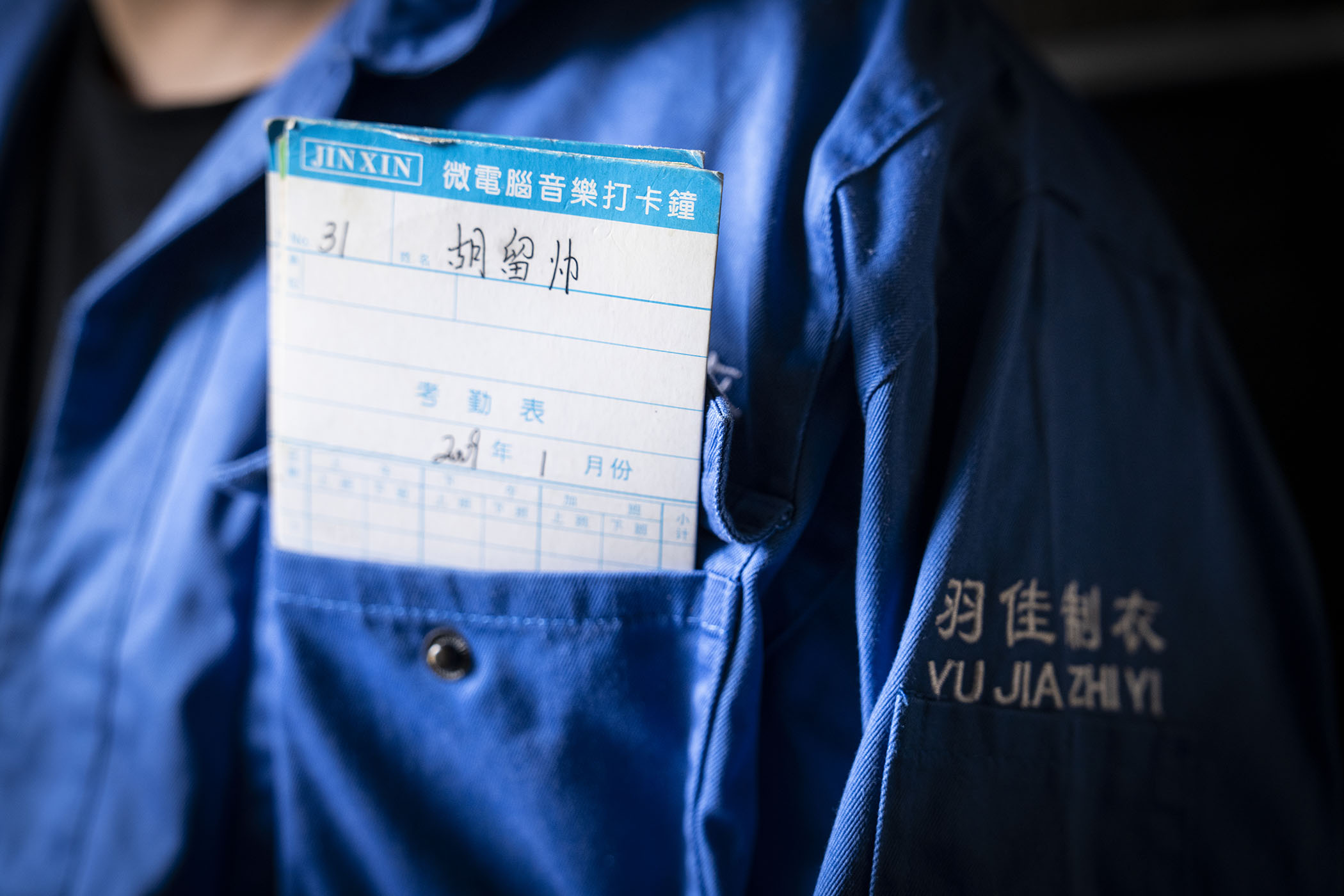Xiao in his former factory jacket with the time card he used to log his hours