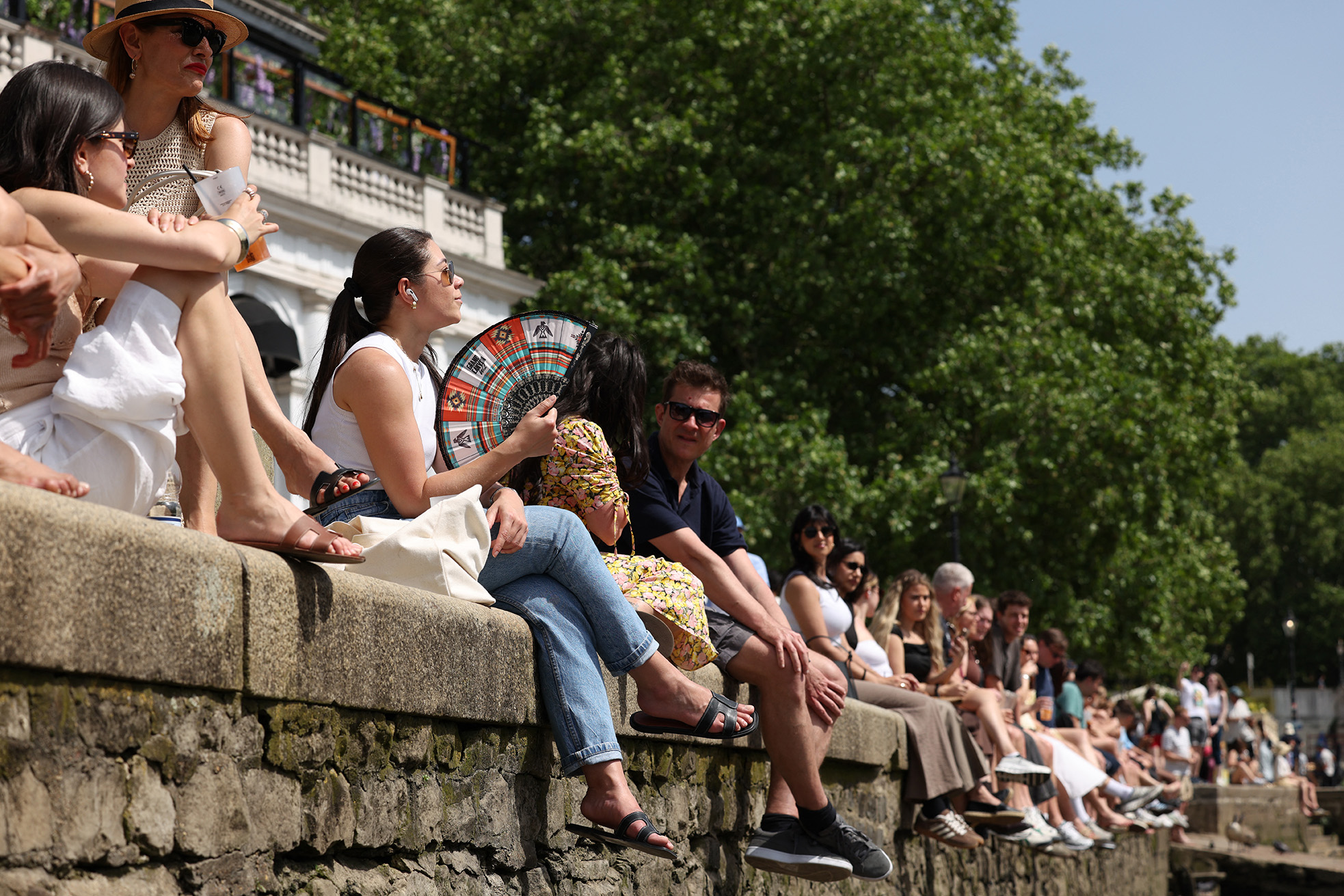 People bask in the sunshine beside the River Thames