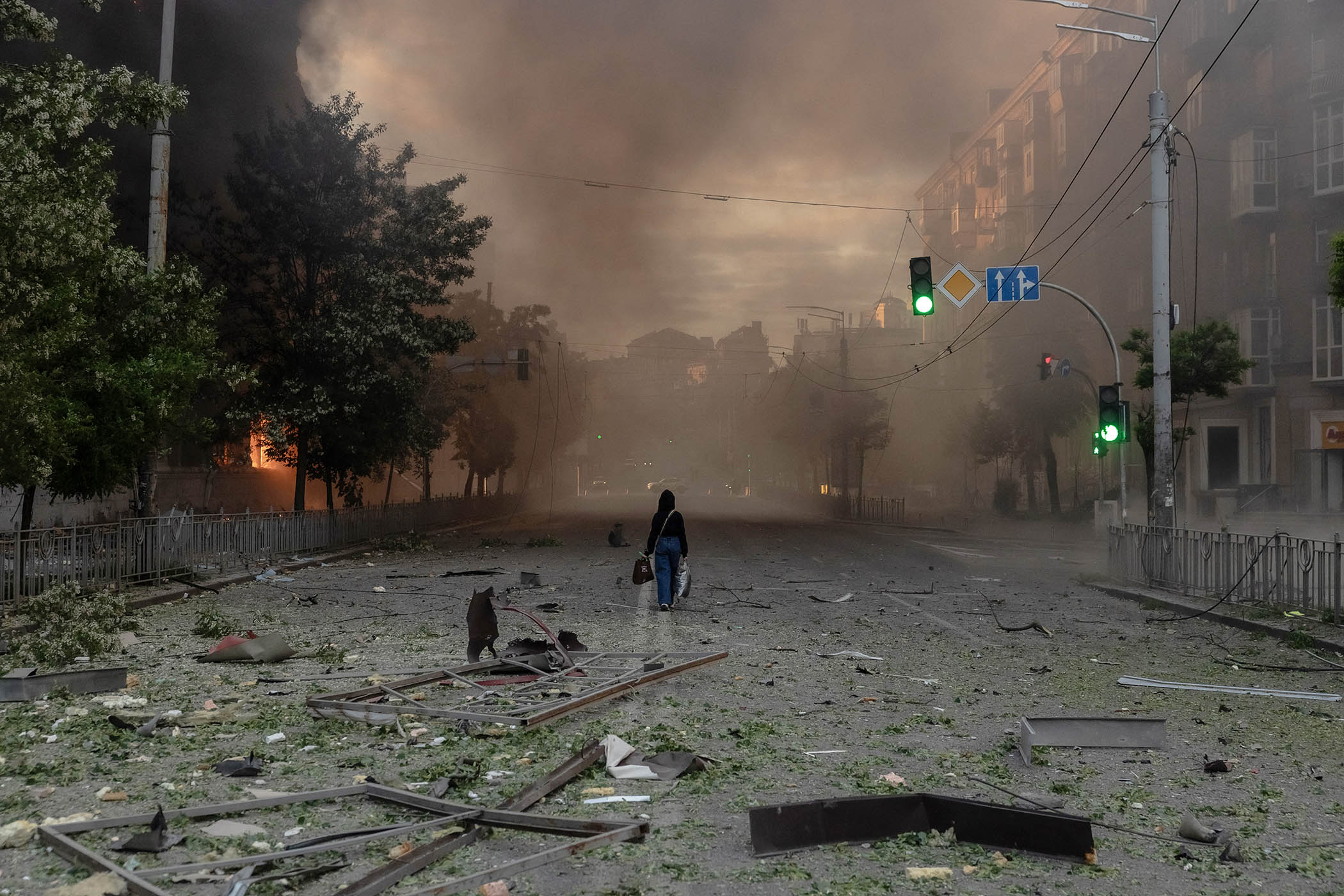 A woman walks along a smoke-filled road beside heavily damaged buildings following Russian strikes in Kyiv